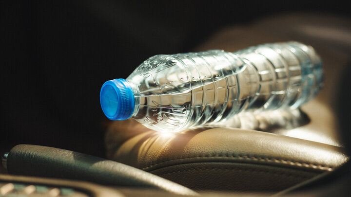 Plastic water bottle with blue cap resting on tan leather car seat.